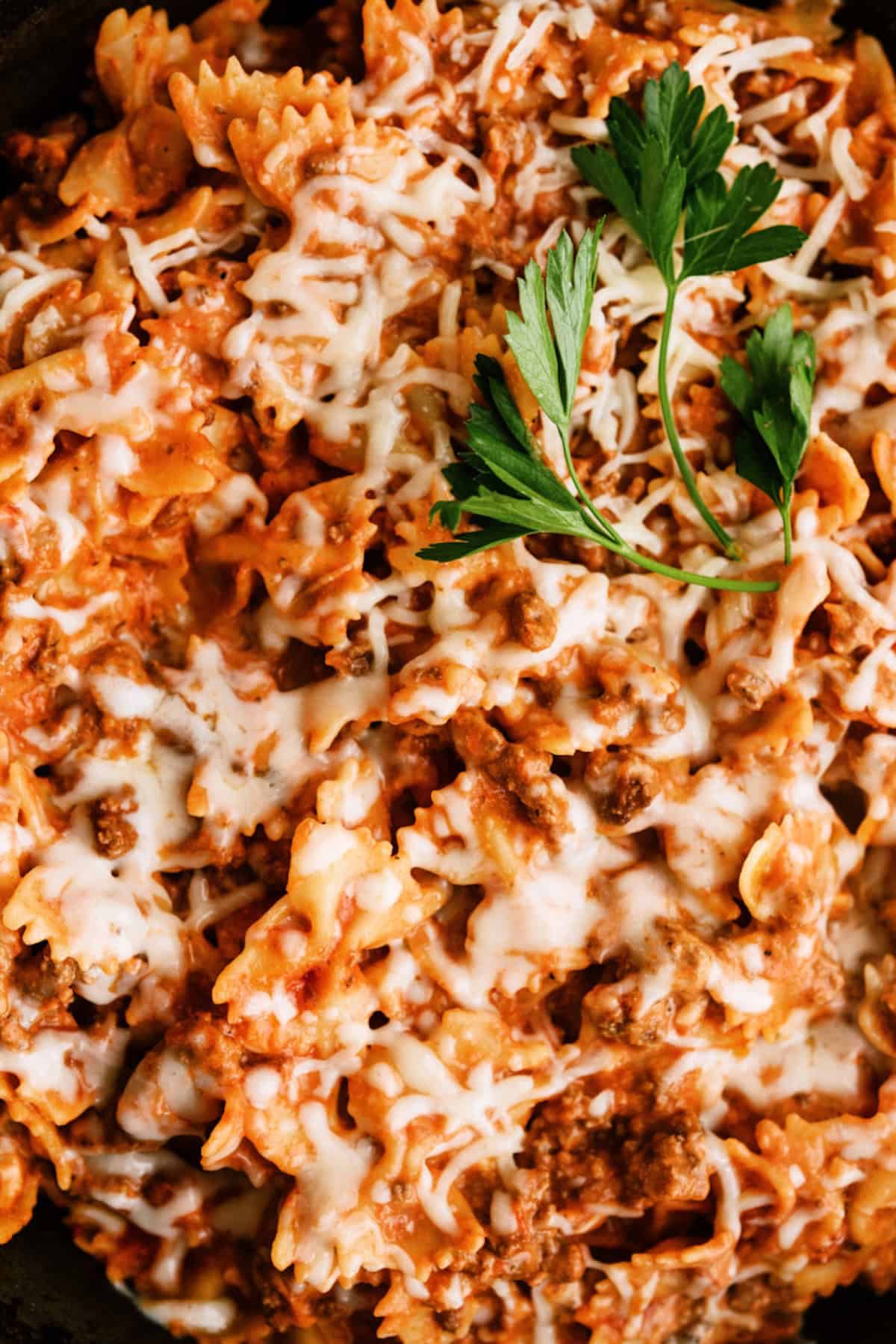 Close-up of cooked pasta with ground meat in tomato sauce, topped with melted cheese and garnished with fresh parsley.