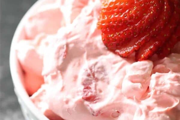 A white bowl filled with strawberry fluff salad, topped with a sliced strawberry.