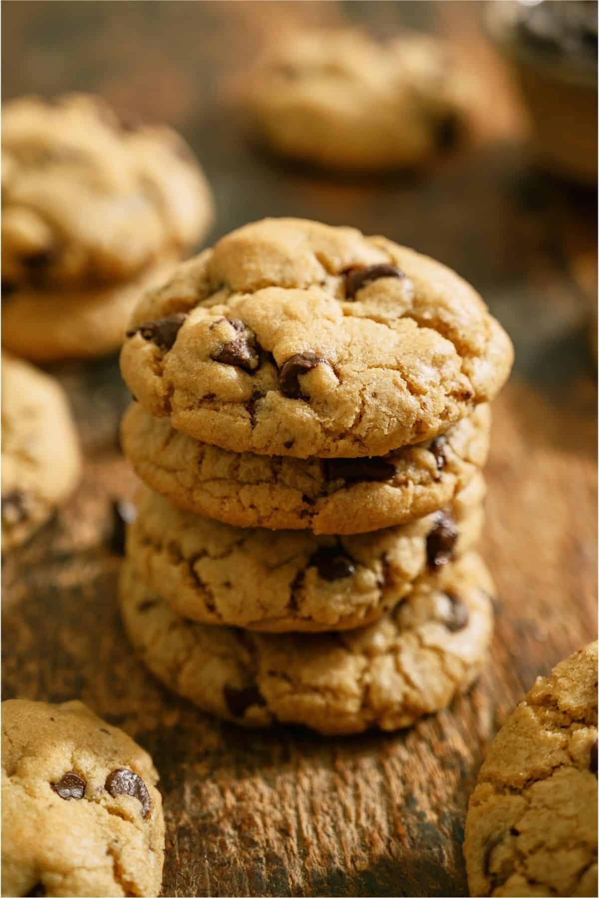 4 Chewy Chocolate Chip Cookies stacked on a wooden table.