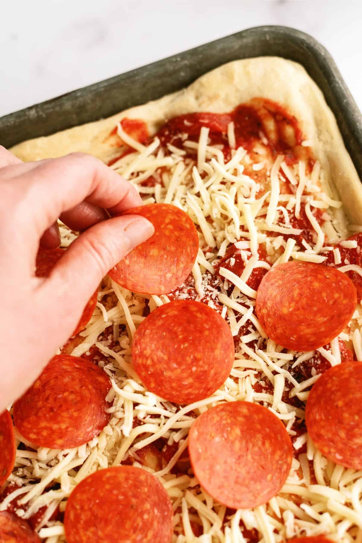 Adding pepperoni on top of cheese on Easy Sheet Pan Pizza