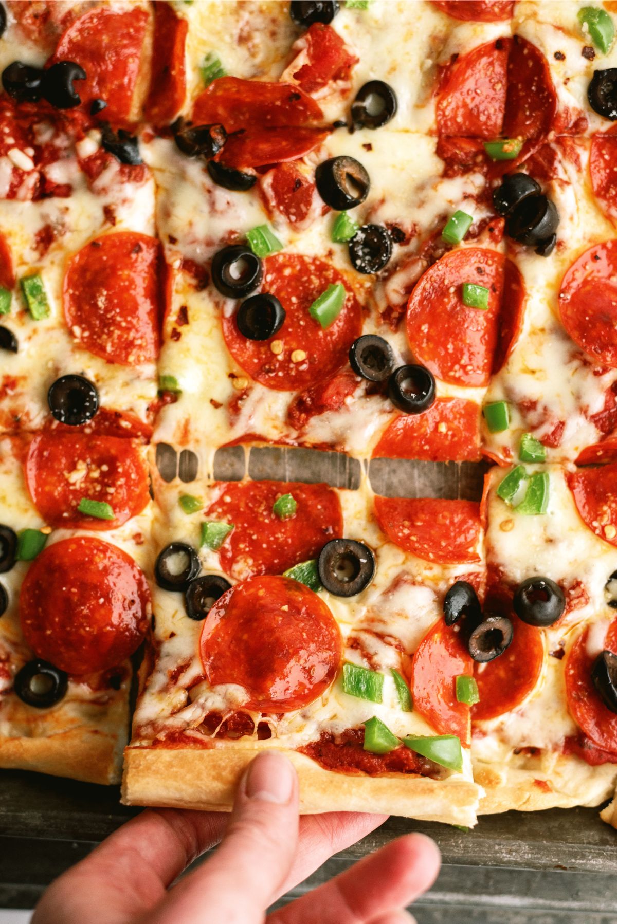 Easy Sheet Pan Pizza cut into squares with one person taking a piece