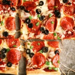 A close-up of a rectangular pepperoni pizza topped with black olives and green bell peppers, divided into square slices.
