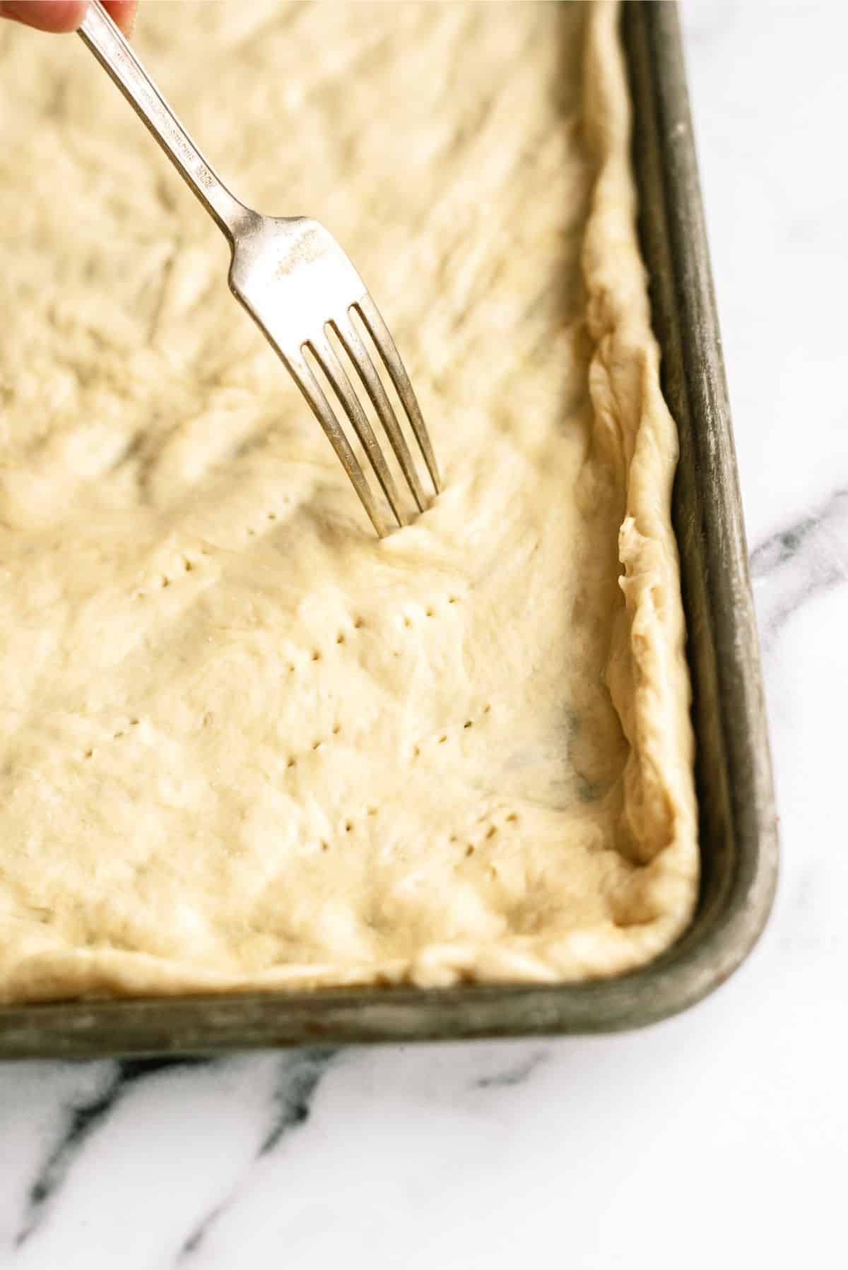 Fork poking holed in unbaked pizza crust