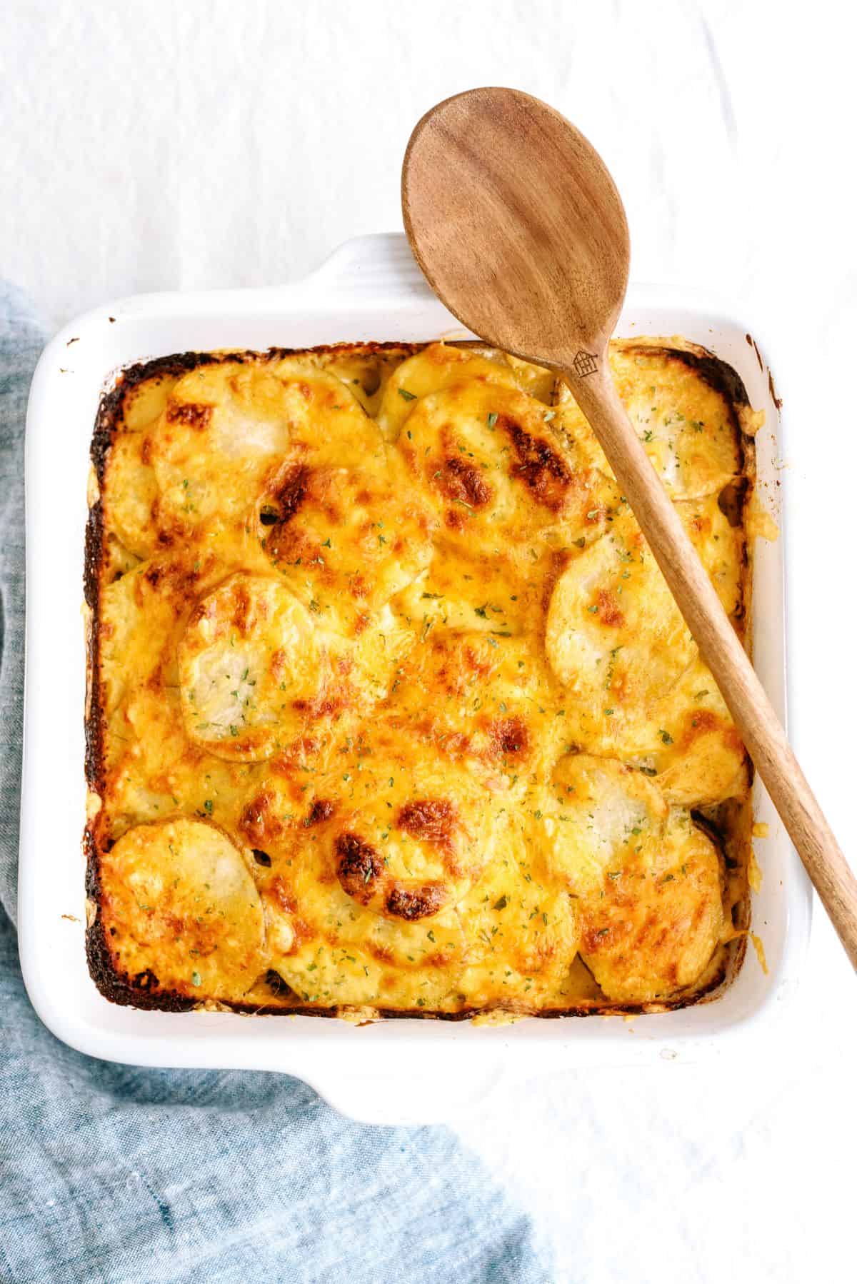 A pan of Homemade Scalloped Potatoes with a wooden spoon