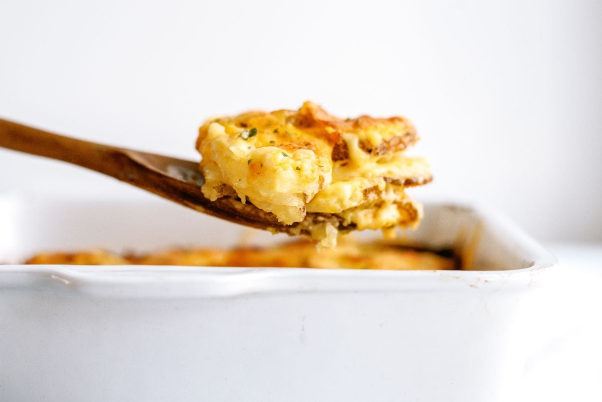 Side view of a pan of Homemade Scalloped Potatoes with a scoop taken out with a wooden spoon