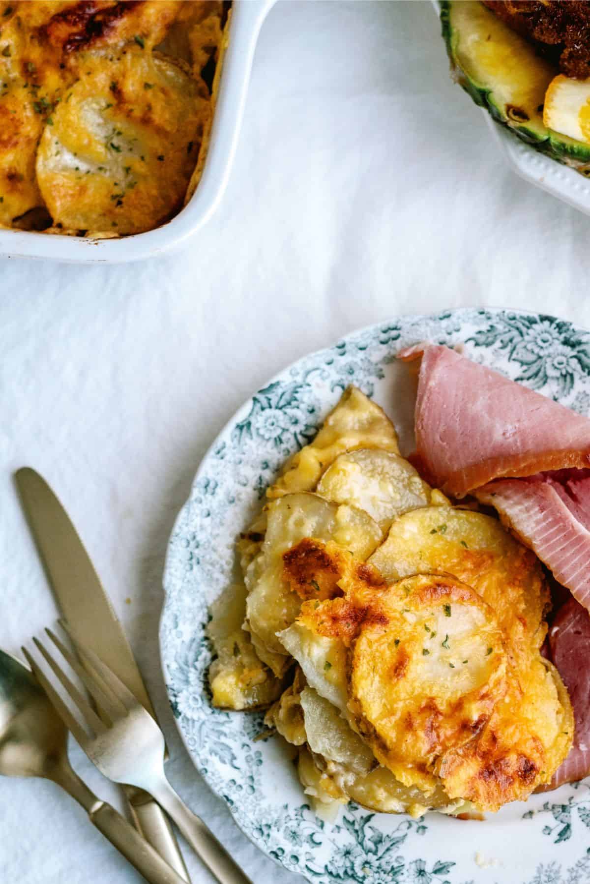 A plate with a serving of Homemade Scalloped Potatoes and ham