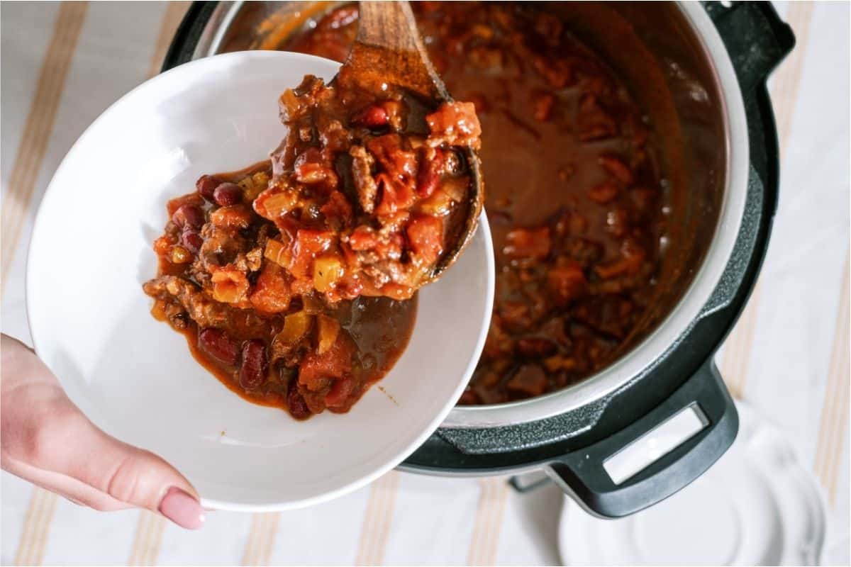 A wooden spoon lifting a serving of Instant Pot Chili (Dump and Go) out of the instant pot into a bowl.
