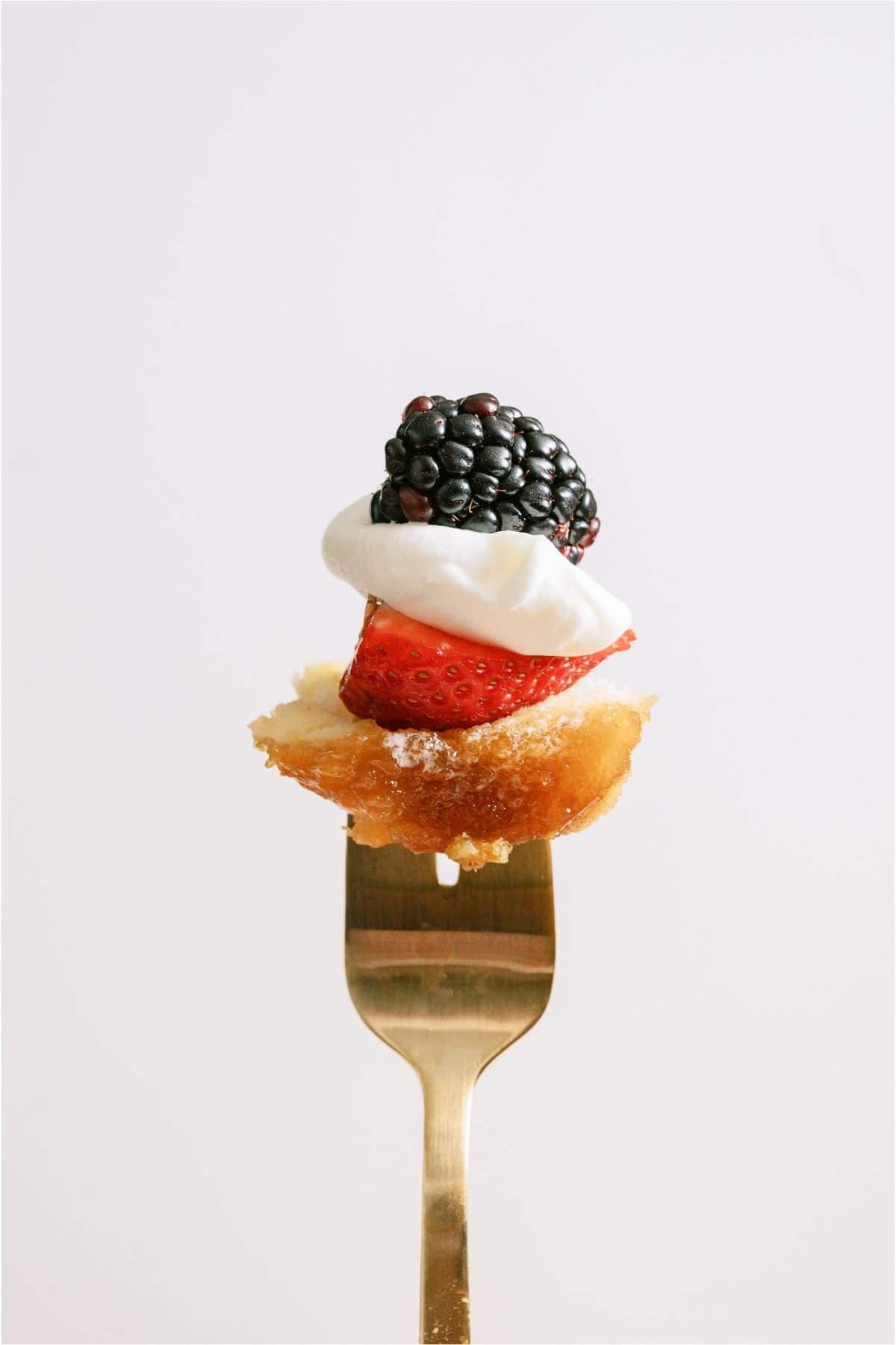 A fork holding a piece of French toast, berries and whip cream.