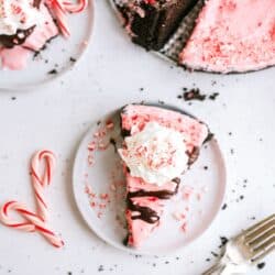 Top view of a slice of Peppermint Crunch Ice Cream Pie on a plate next to candycanes with the remaining pie in the background.