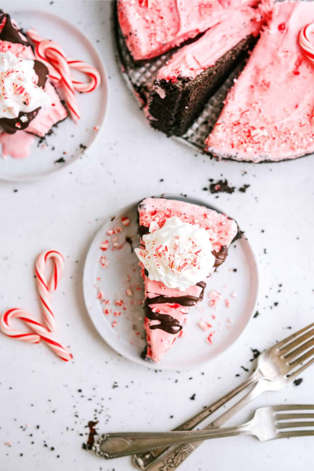 Top view of a slice of Peppermint Crunch Ice Cream Pie on a plate next to candycanes with the remaining pie in the background.