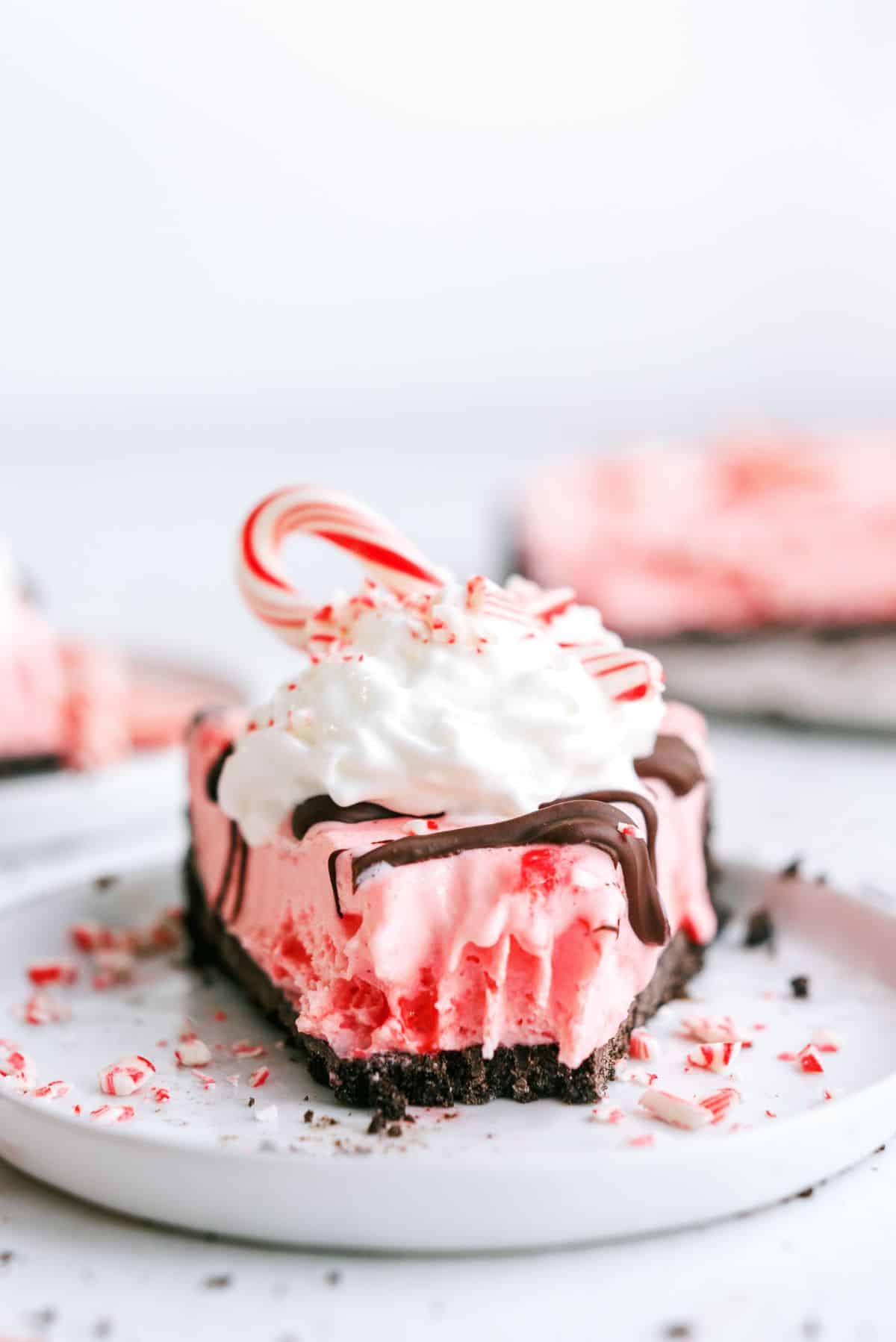 Front view of a slice of Peppermint Crunch Ice Cream Pie on a plate with a bite missing out of it.