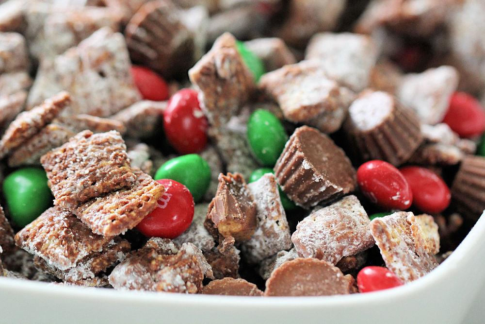 Christmas Muddy Buddies with colorful candies and Reese's peanut butter cups in a white bowl