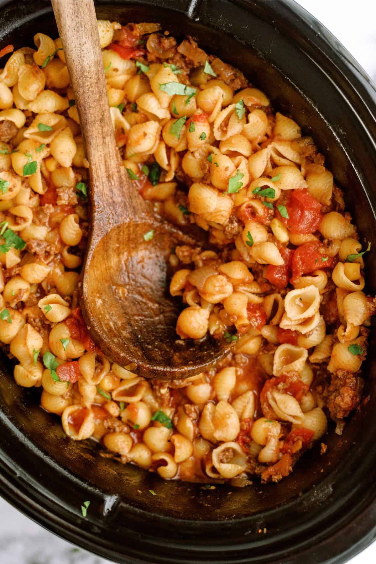 Slow Cooker Cheesy Beef Taco Pasta in slow cooker with a wooden spoon