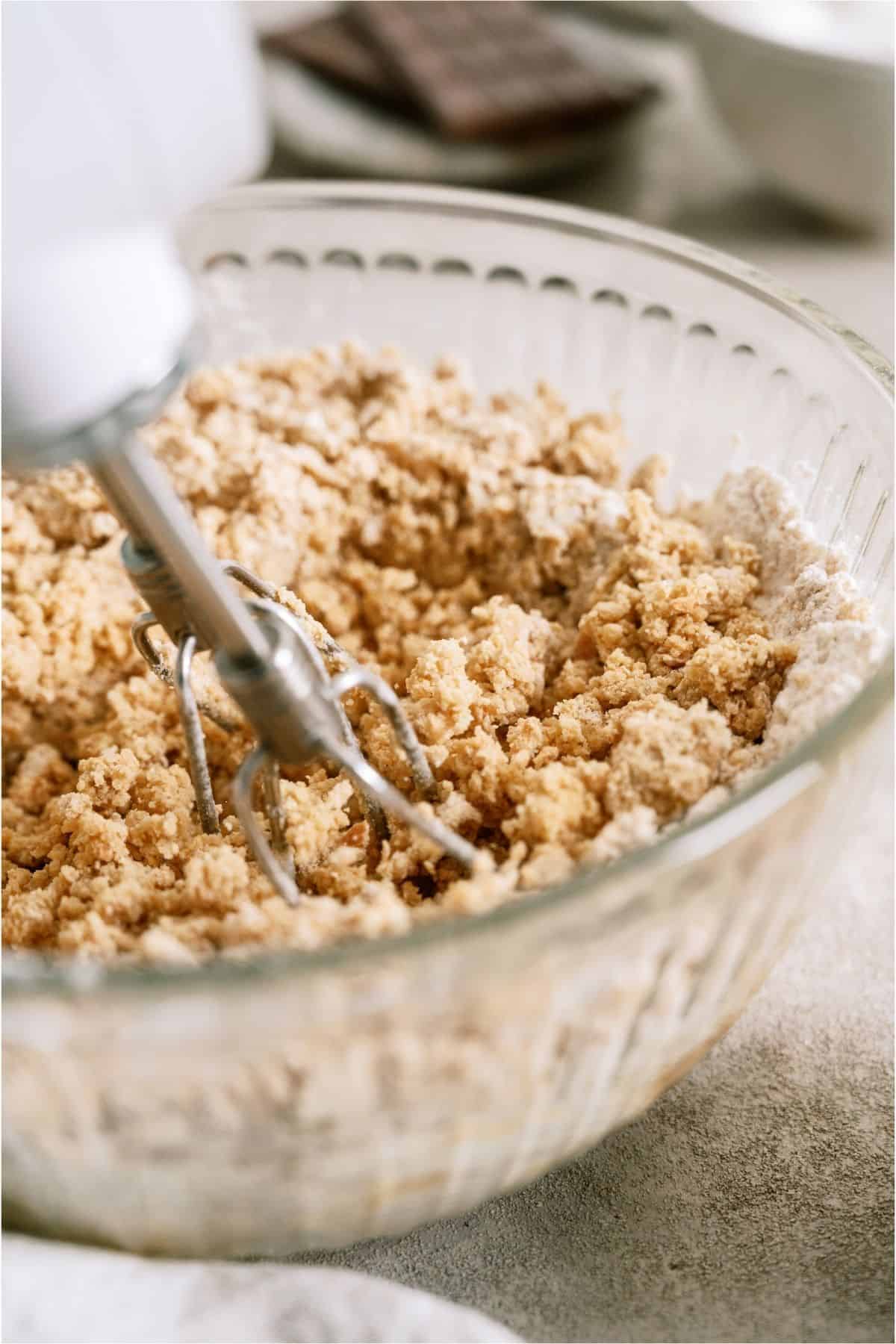A hand mixer combining S’mores Cookie dough in a glass mixing bowl.
