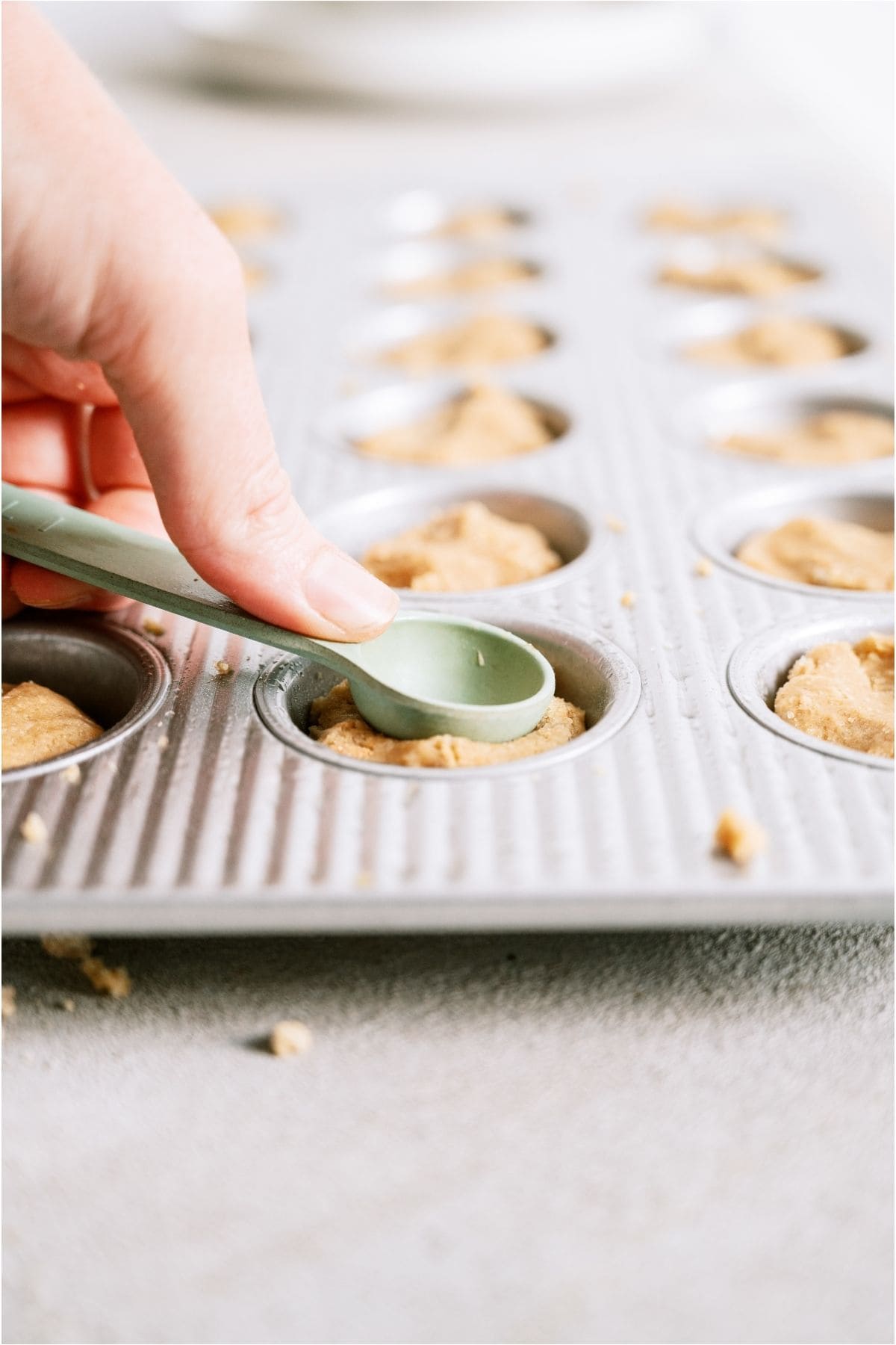 A spoon pressing the middle of the cookie dough to make an indent.