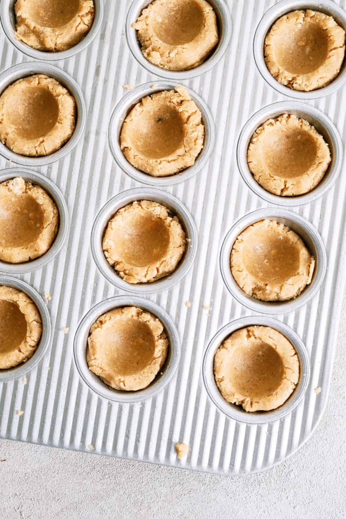 A mini muffin tin with cookie dough cups in each tin with the center indented.