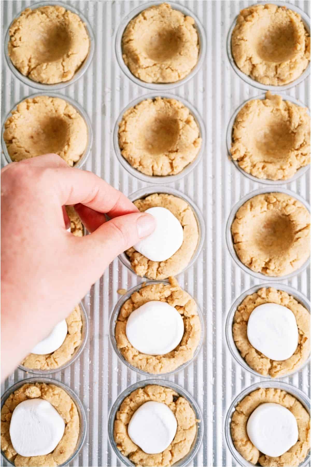 Placing a marshmallow in each indented cookie cup.