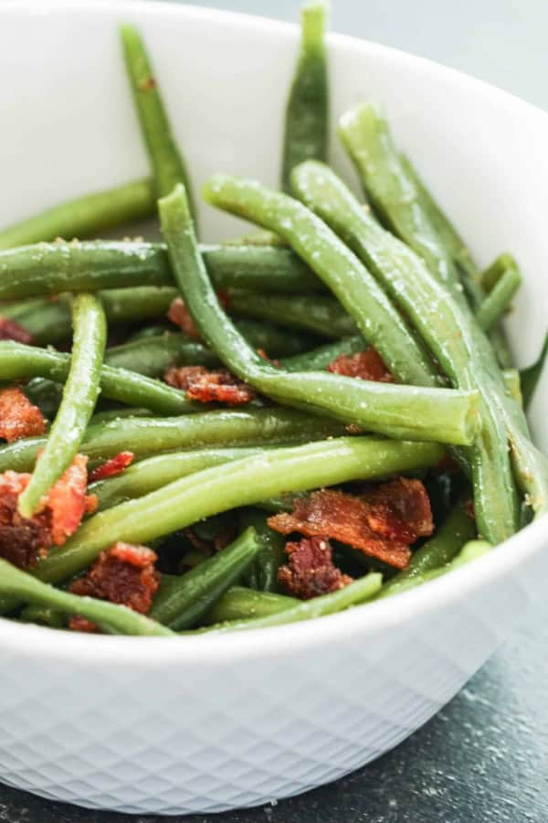 A white bowl filled with cooked green beans and pieces of crispy bacon.