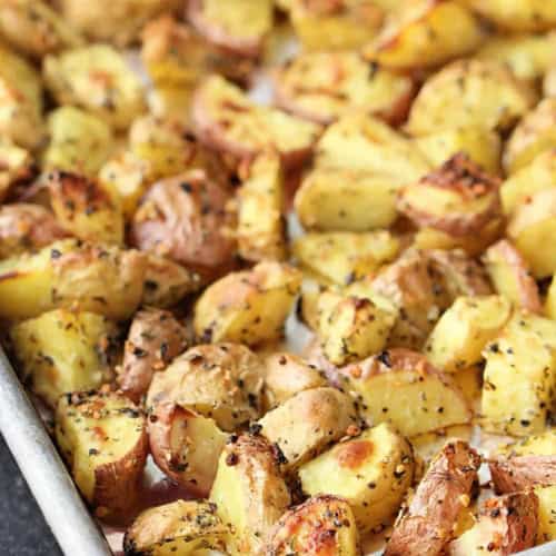 A baking tray filled with roasted, seasoned potato chunks, browned and crispy on the edges.