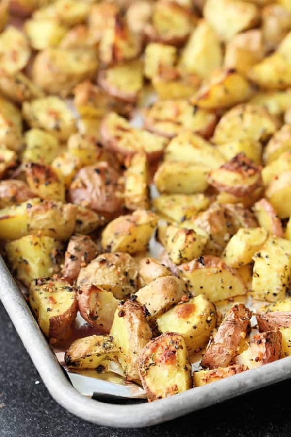 A baking tray filled with roasted, seasoned potato chunks, browned and crispy on the edges.