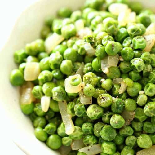 A white bowl filled with cooked green peas mixed with diced onions and seasoned with black pepper.