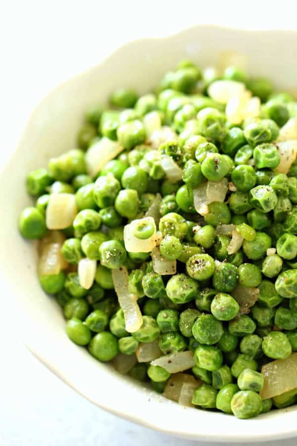 A white bowl filled with cooked green peas mixed with diced onions and seasoned with black pepper.
