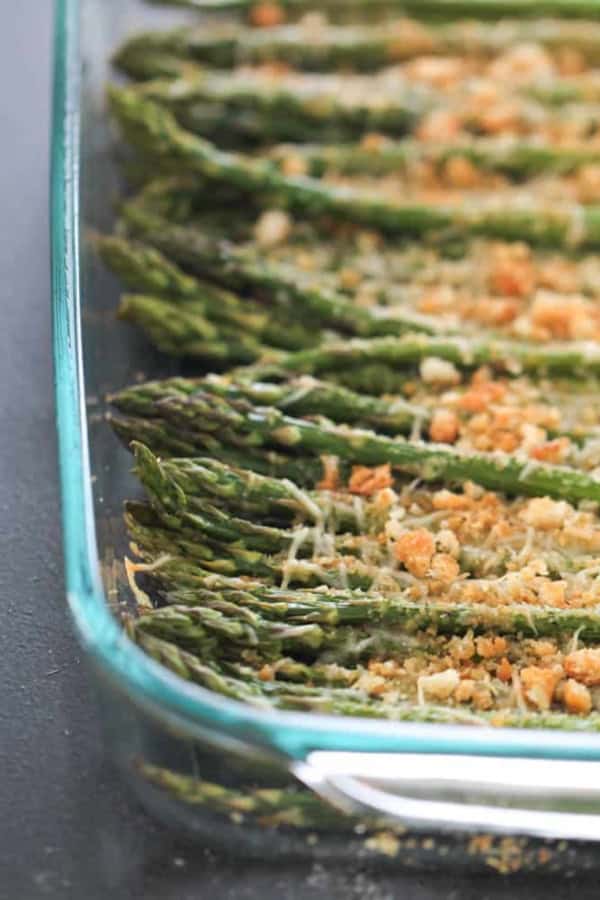 Glass dish containing roasted asparagus spears topped with breadcrumbs and grated cheese.