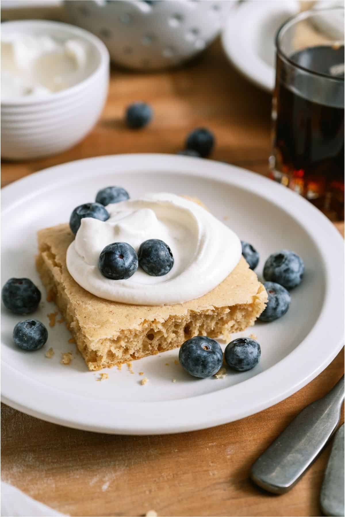 A serving of Baked Pancakes on a white plate topped with whip cream and blueberries.