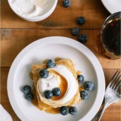 A slice of Baked Pancakes on a white plate topped with berries, whip cream and syrup.