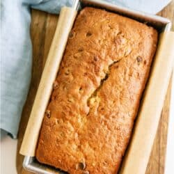 A loaf of Chocolate Chip Banana Bread in a pan on a cutting board.