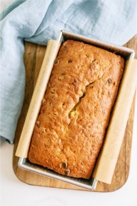 A loaf of Chocolate Chip Banana Bread in a pan on a cutting board.
