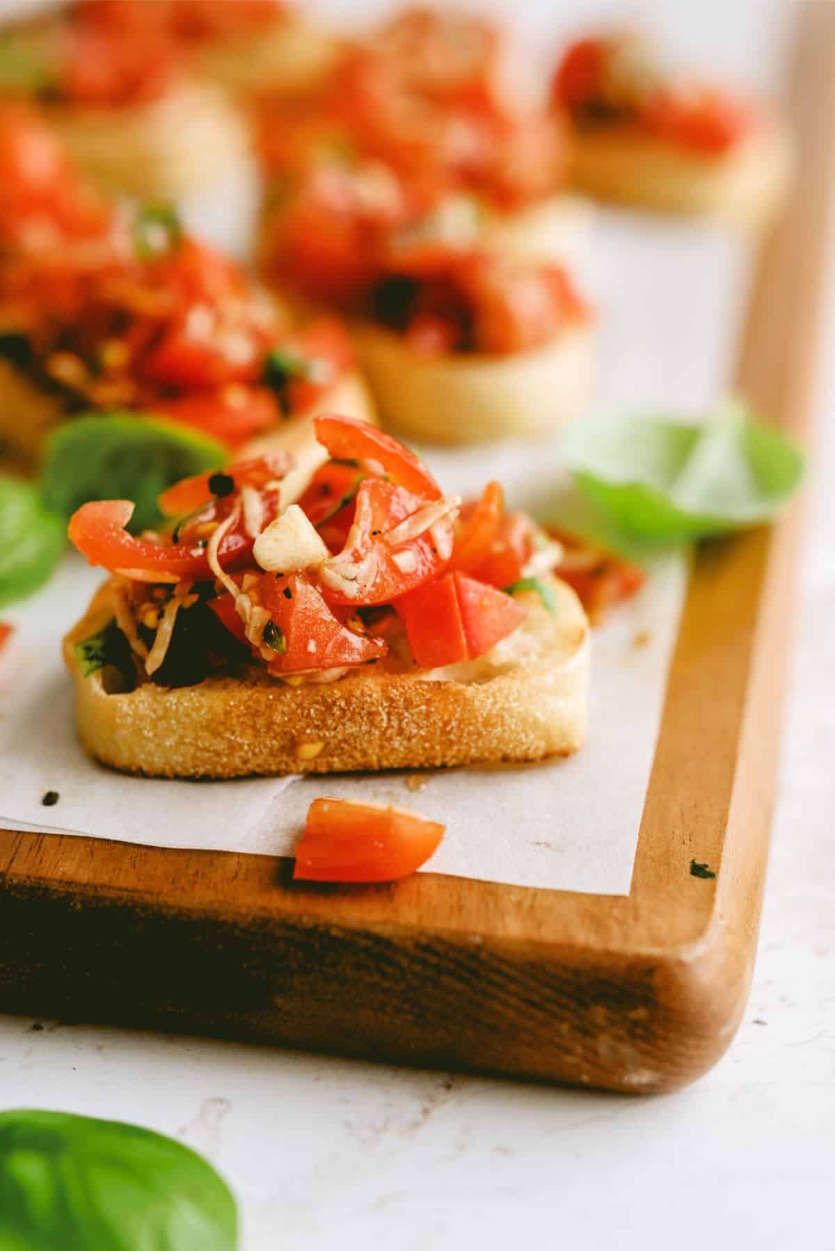 Close-up of bruschetta topped with diced tomatoes and herbs, served on parchment paper on a wooden board.