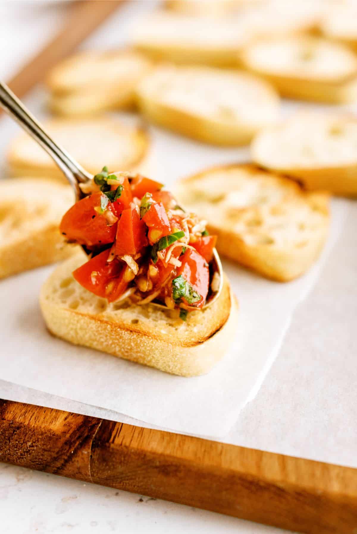 Slice of baguette topped with diced tomatoes, basil, and garlic on parchment paper.