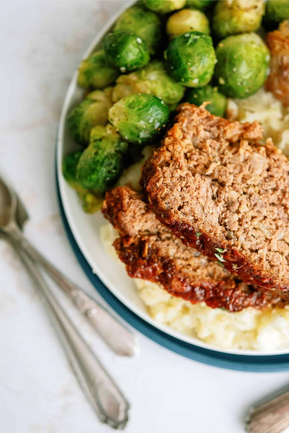 A plate with two slices of Grandma A’s Meatloaf with a side of brussels sprouts