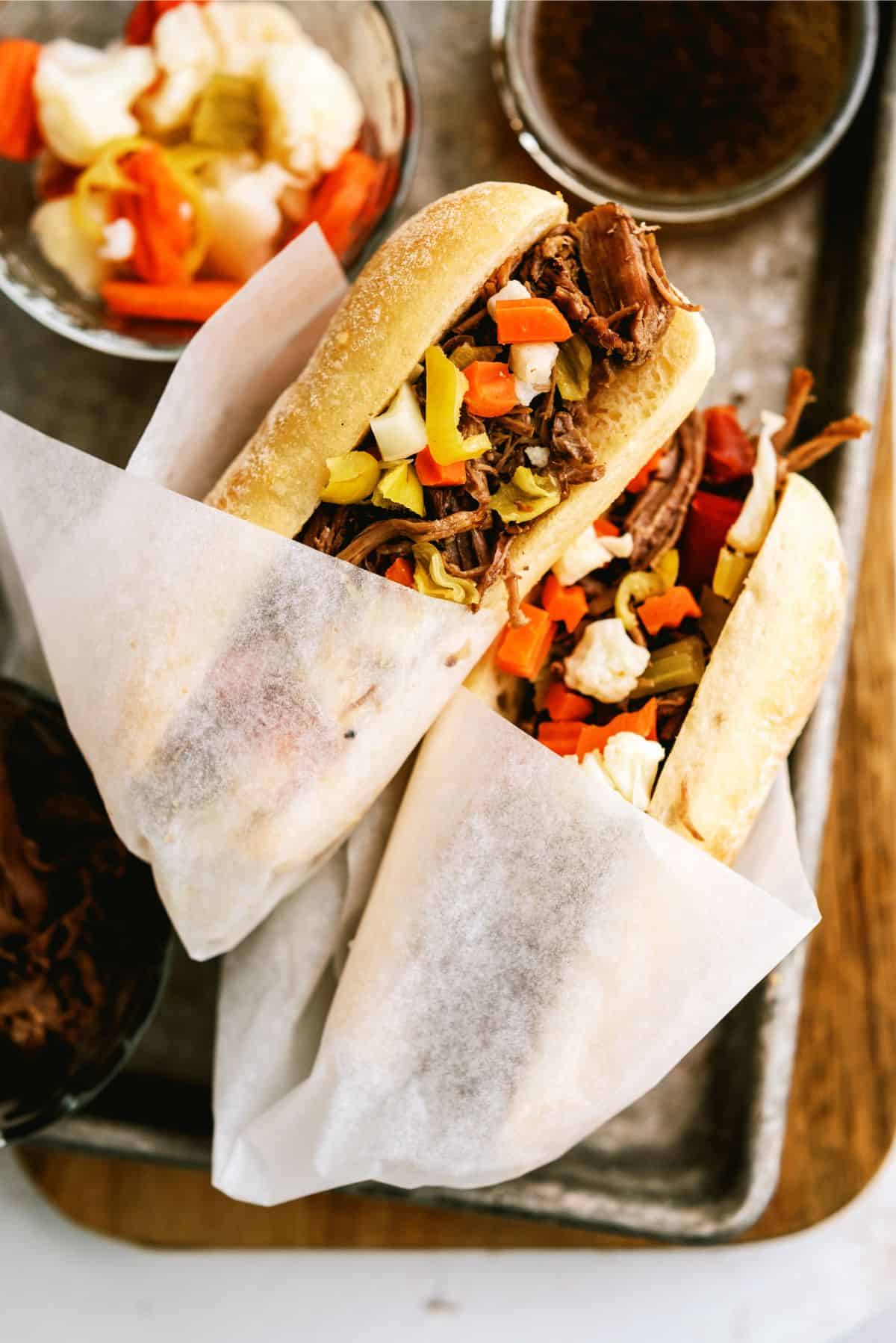 2 Instant Pot Chicago-Style Italian Beef Sandwiches on a sheet pan with a side of juice for dipping