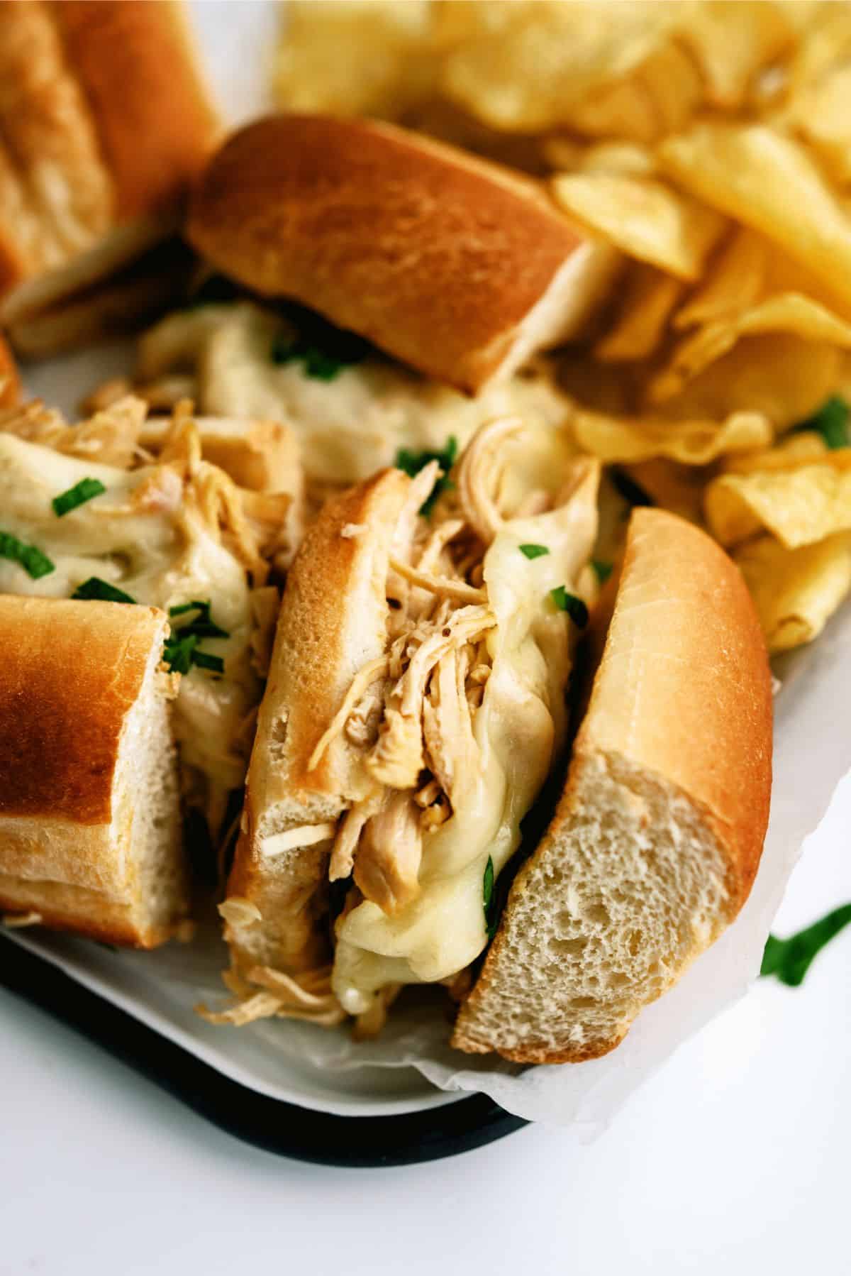 Close up of a platter of Instant Pot Chicken French Dip Sandwiches with a side of chips