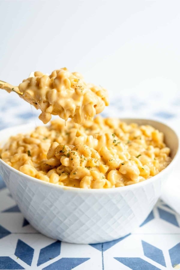 A white bowl filled with creamy macaroni and cheese, with a fork holding a bite above the bowl.