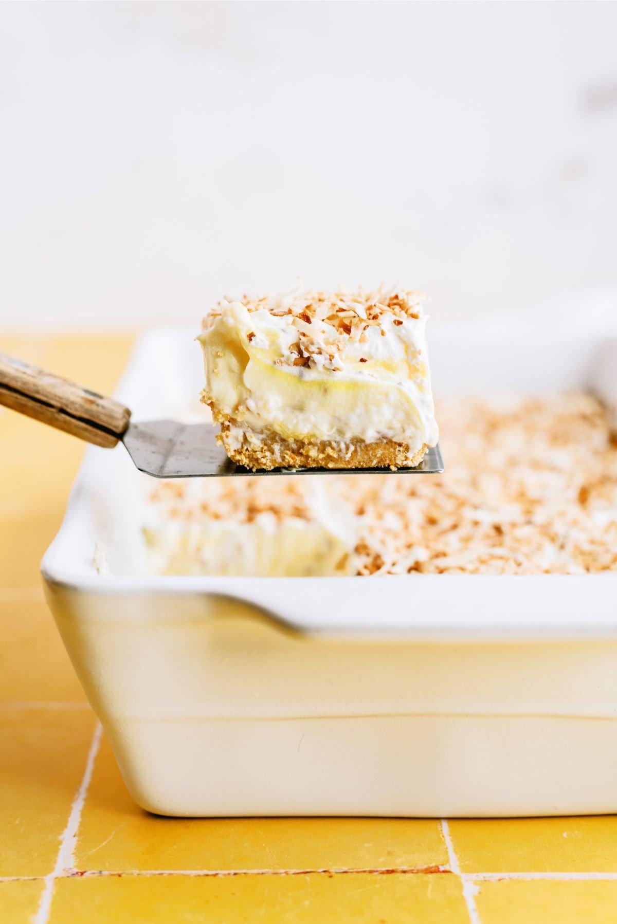 A pan of Layered Pina Colada Dessert Recipe (Lush) with a square being lifted out