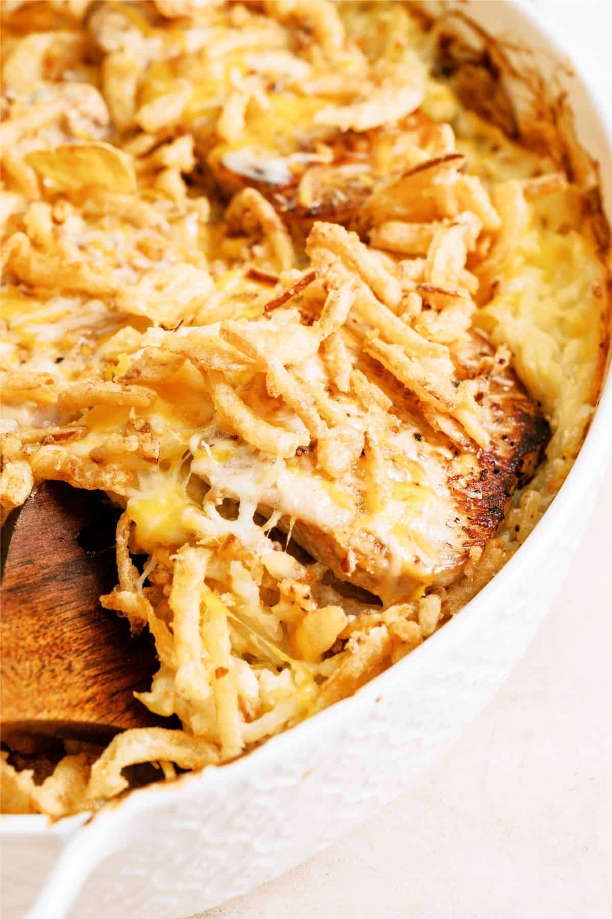 A wooden spoon lifting a scoop of Pork Chop Casserole With Hashbrowns out of the dish,