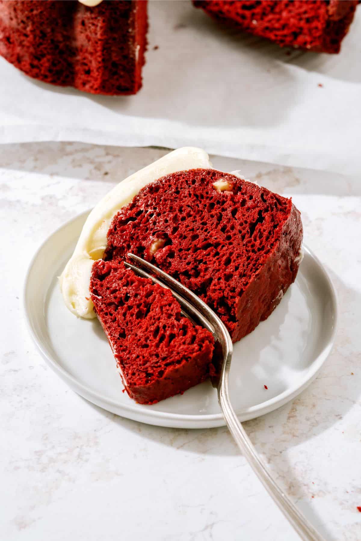 A slice of Red Velvet Bundt Cake on a plate with a fork slicing into it.