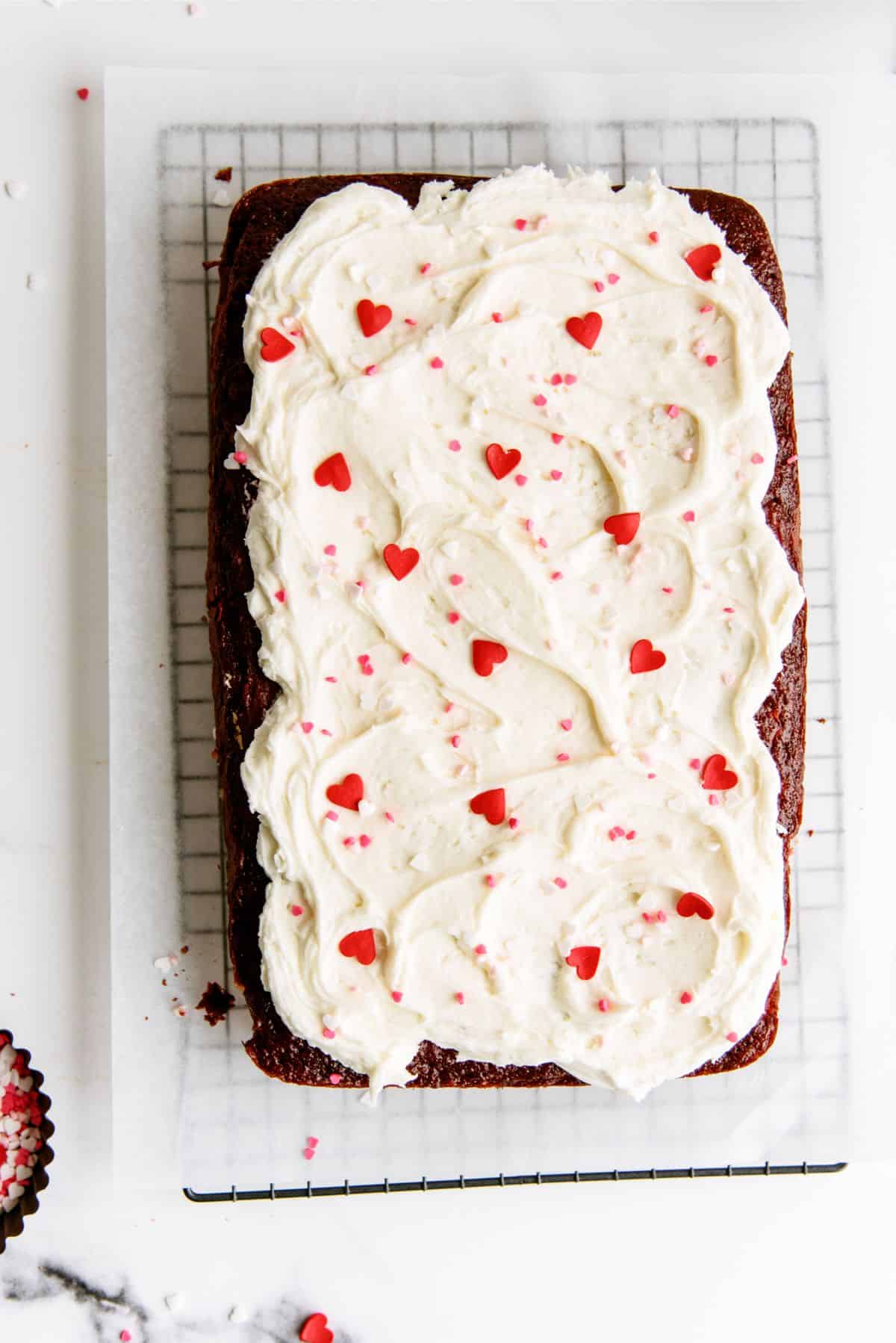 Red Velvet Cheesecake Swirl Cake topped with frosting and candy hearts on a cooling rack