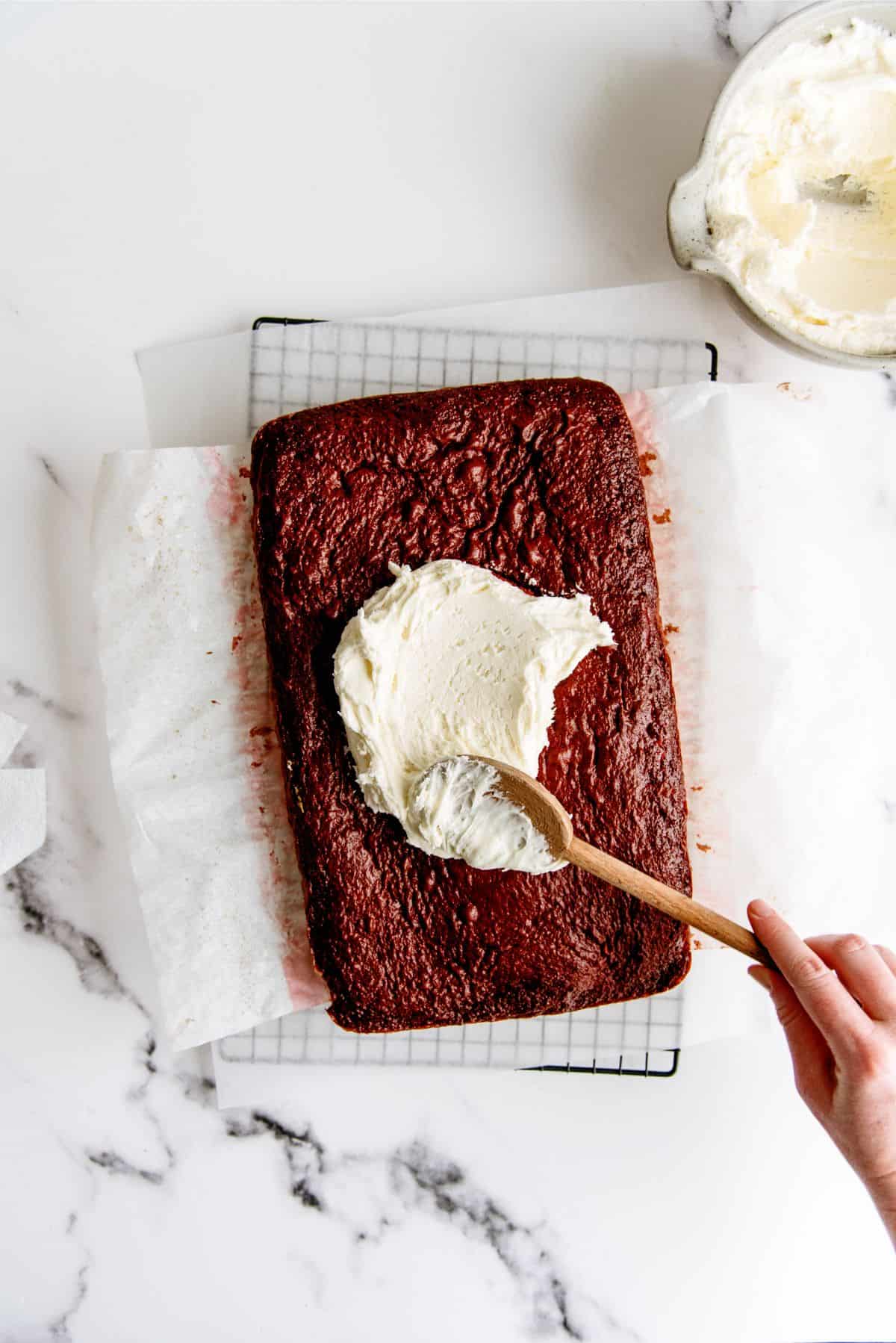 Red Velvet Cheesecake Swirl Cake with a dollop of frosting on it. spread by a wooden spoon