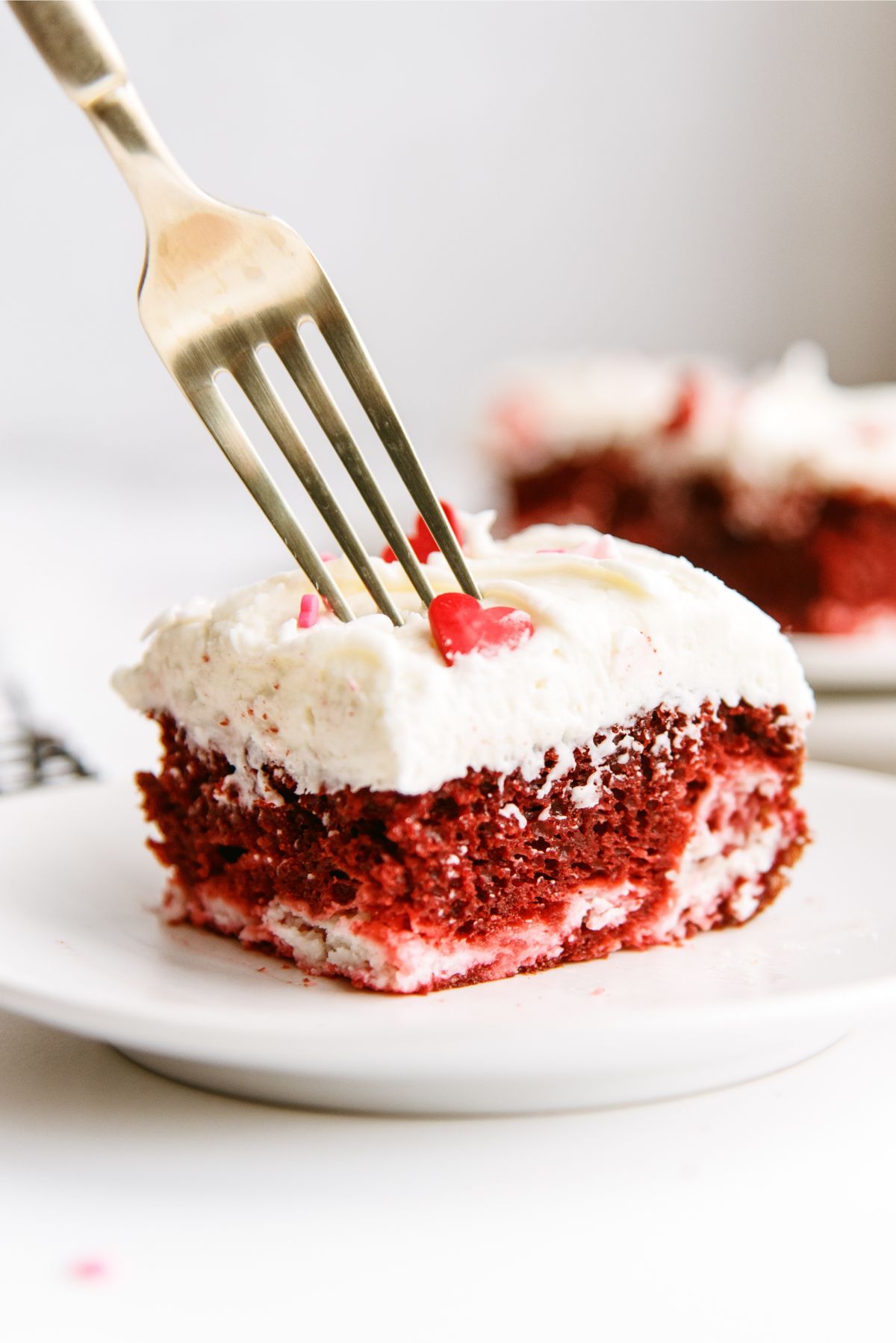 A slice of Red Velvet Cheesecake Swirl Cake on a plate with a fork ready to take a bite