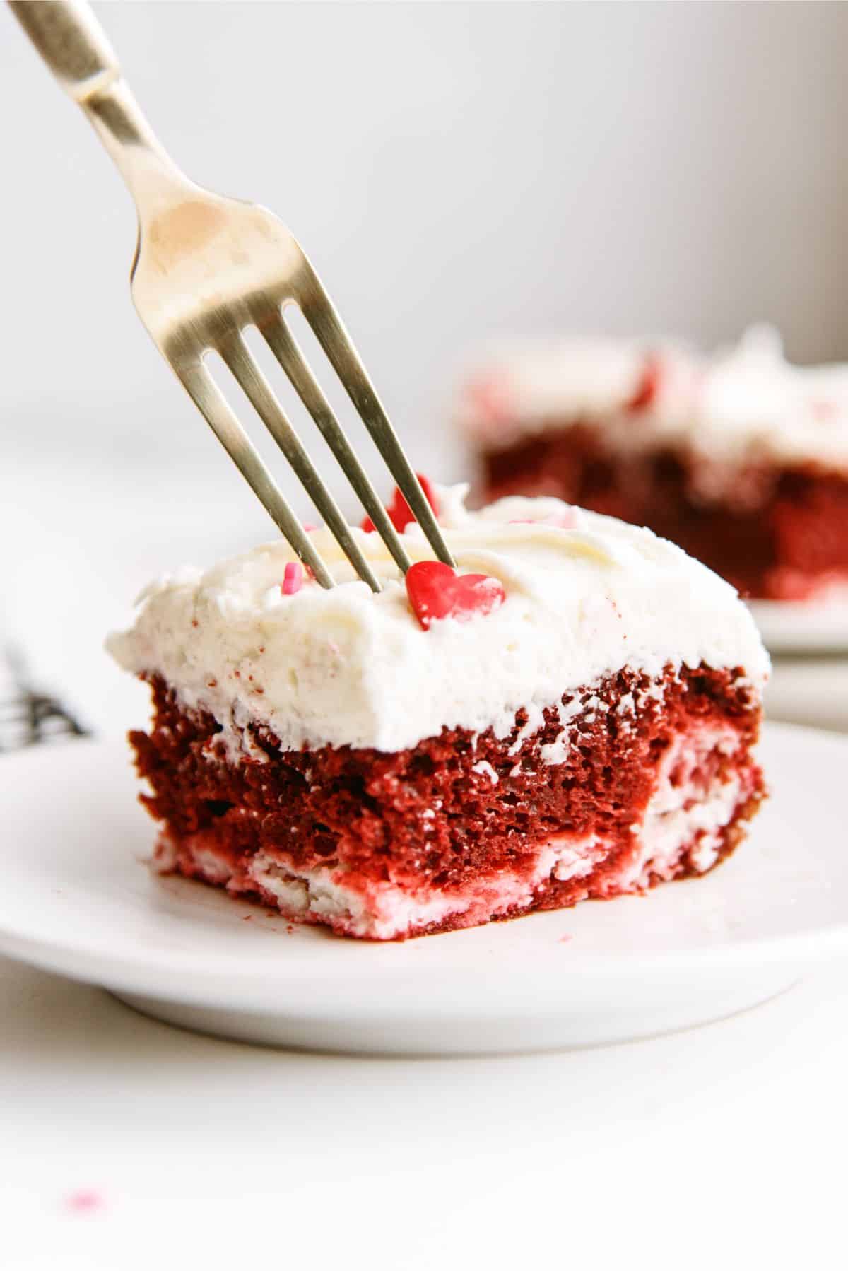 A slice of Red Velvet Cheesecake Swirl Cake on a white plate with a fork.