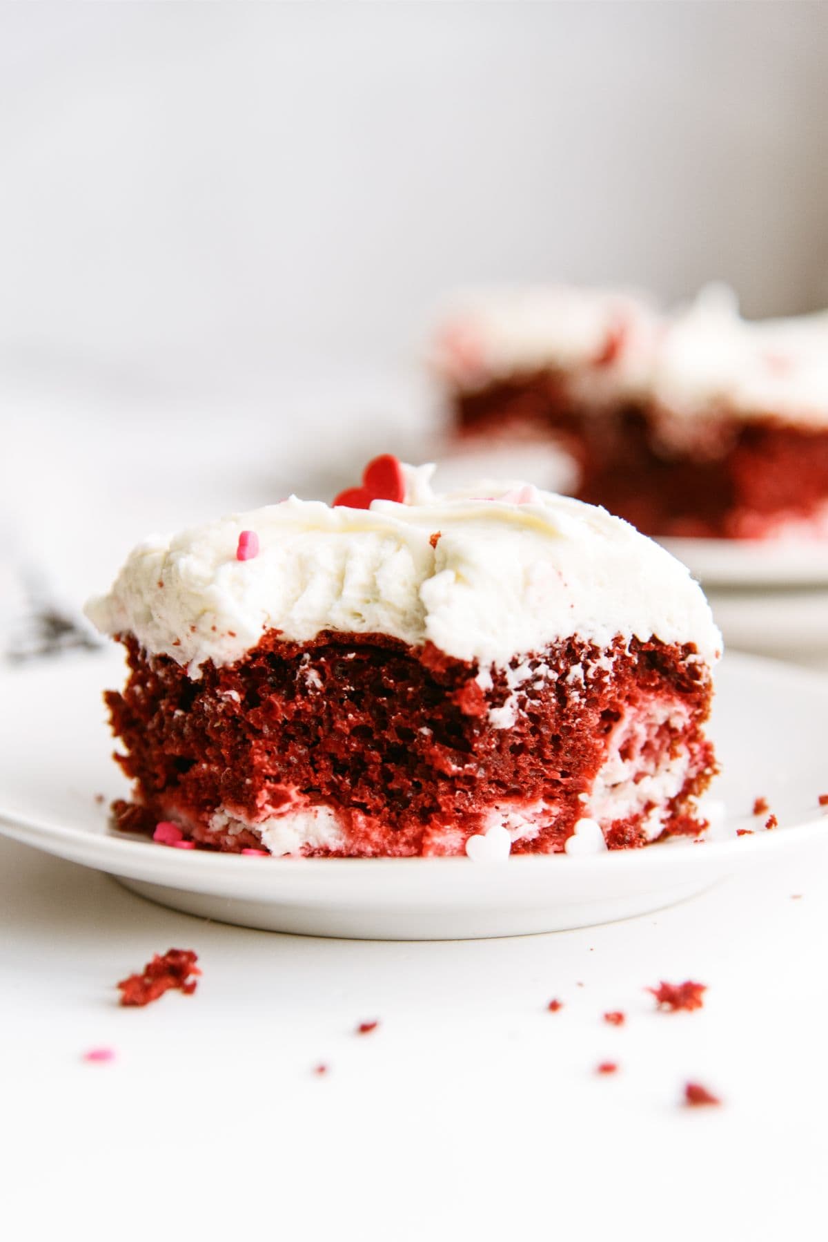 A slice of Red Velvet Cheesecake Swirl Cake on a white plate with a bite missing.
