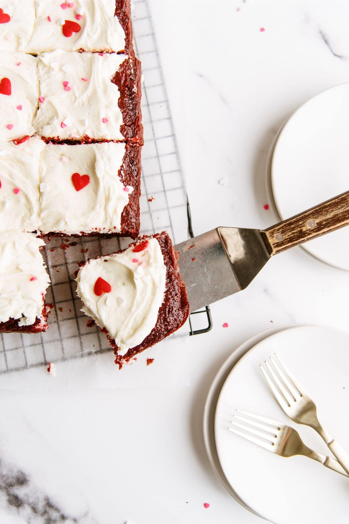 Top view of Red Velvet Cheesecake Swirl Cake frosted and cut into squares with a spatula lifting one serving