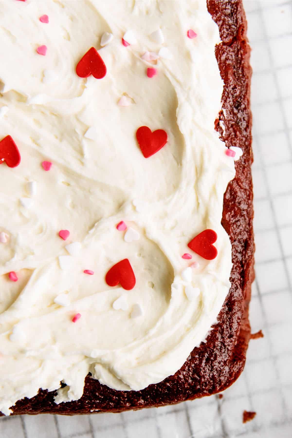 Top view close up of Red Velvet Cheesecake Swirl Cake, frosted with sprinkles, on a cooling rack