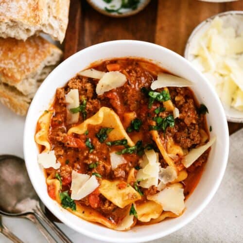A bowl of hearty lasagna soup garnished with chopped herbs and shaved Parmesan cheese. T