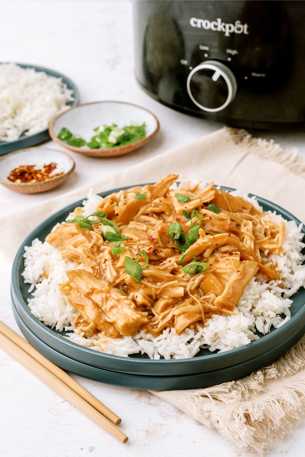 Slow Cooker Bourbon Chicken on top of a plate of rice with a slow cooker in the background