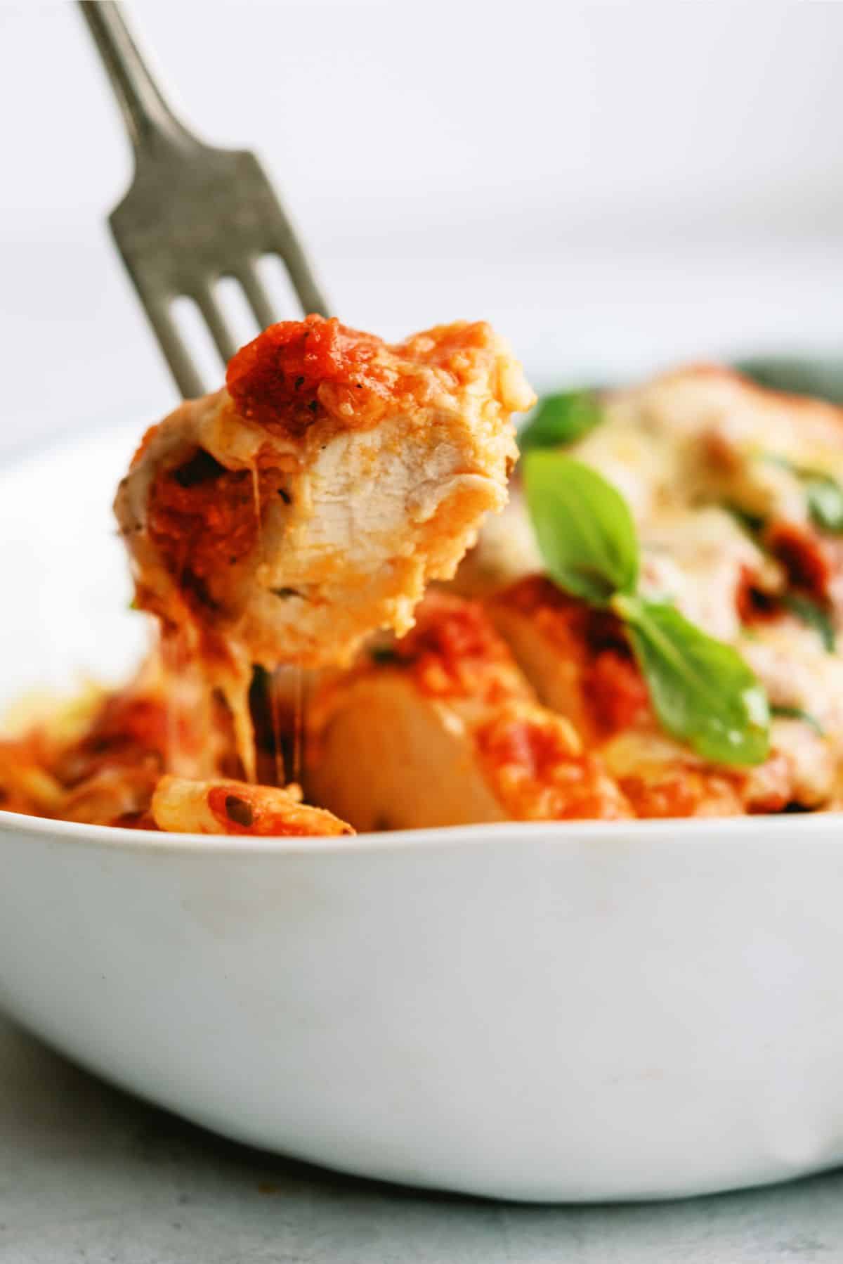 a fork with a bite of a Slow Cooker Chicken Parmesan breast in a bowl